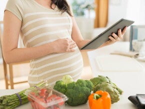 Вагітна жінка з планшетом готує корисні овочі
