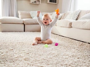 Малыш сидит на коврике и радостно поднимает игрушку