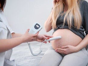 Фото: врач делает УЗИ беременной женщине в серой кофте, датчик на животе