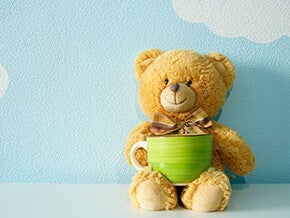 Плюшевий ведмедик тримає чашку на блакитному фоні