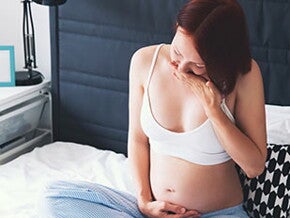 Вагітна жінка сидить на ліжку з рукою на животі