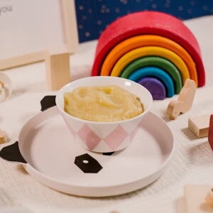 Пюре для дитини в мисці поруч із дитячими іграшками