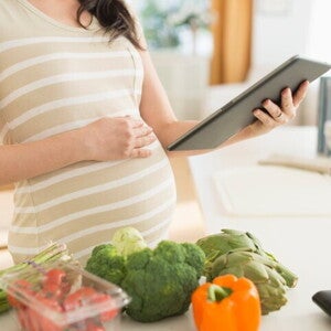 Вагітна жінка з планшетом готує корисні овочі