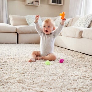 Малюк сидить на килимі та радісно піднімає іграшку