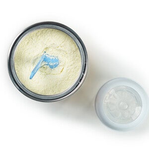 Open container of baby formula with a scoop next to the lid.