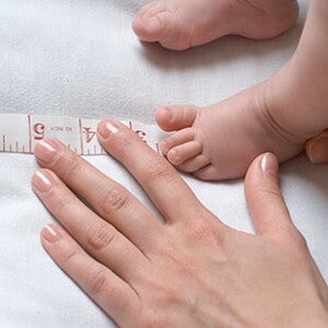 Ніжка немовляти поряд із рукою дорослого та сантиметром