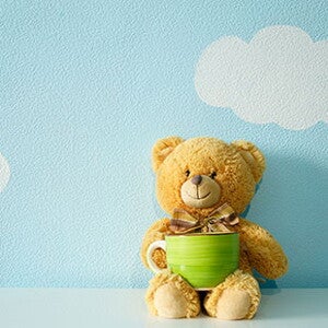 Плюшевий ведмедик тримає чашку на блакитному фоні