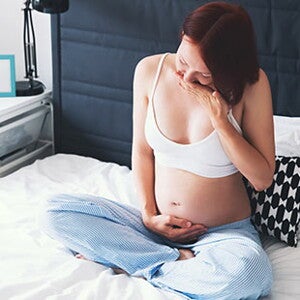 Вагітна жінка сидить на ліжку з рукою на животі