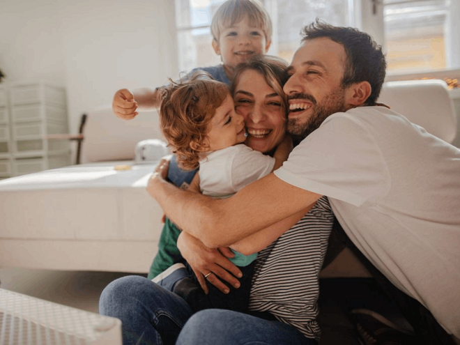 Щаслива родина, що сміється разом на дивані, відображає підтримку Nestlé FamilyNes для батьків.
