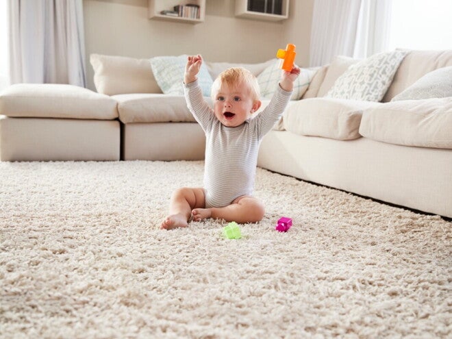 Малыш сидит на коврике и радостно поднимает игрушку
