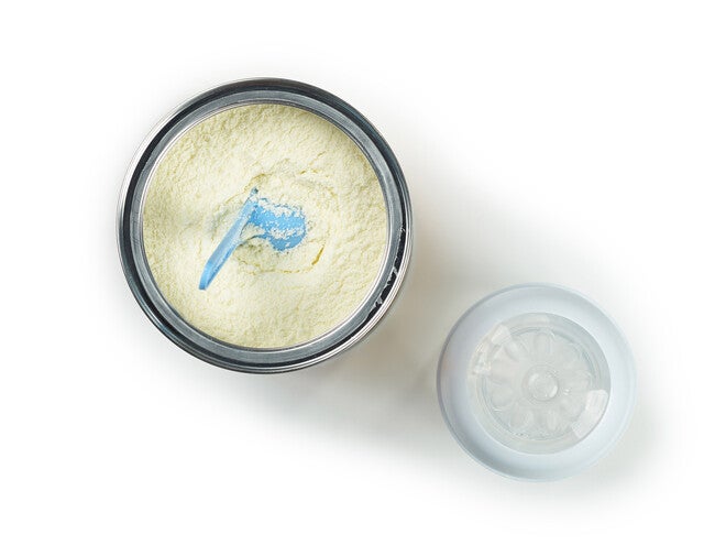 Powdered baby formula with blue scoop and lid on white background.