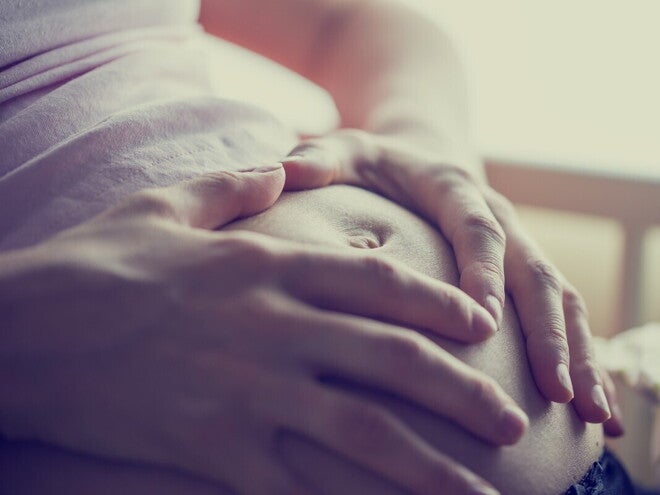 Руки беременной женщины нежно держат живот крупным планом